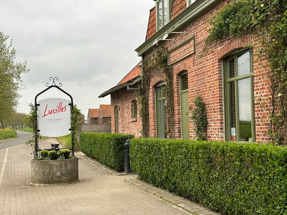 Bakstenen gevel met klimplanten en strakke hagen langs de straat, met het smeedijzeren uithangbord van Lucilles