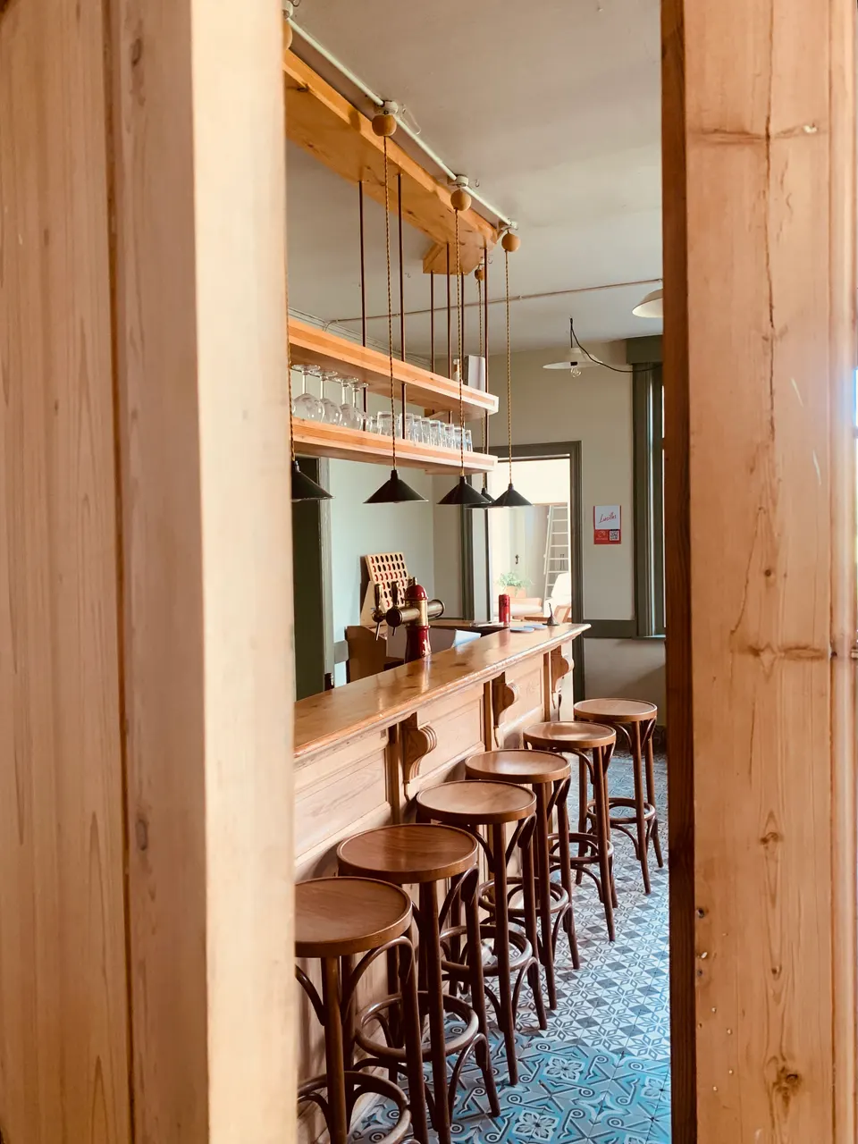 Houten toog met krukken in het café, met glazen op een hangend rek en een vloer van blauwe cementtegels
